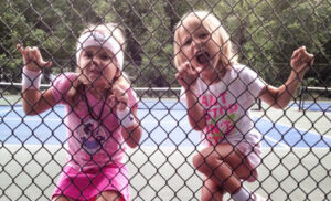 two little girls so excited about tennis that they are climbing the fence 